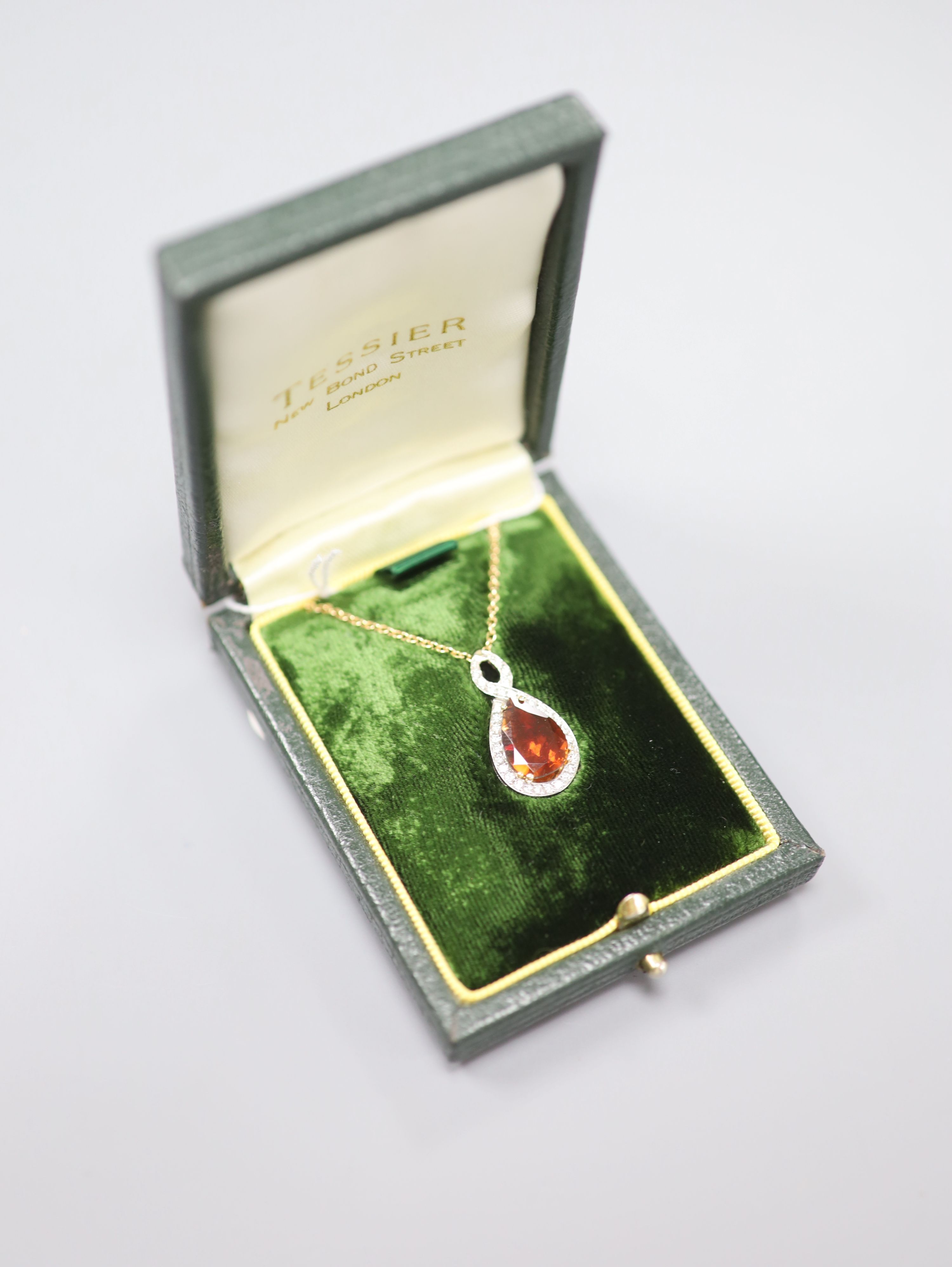 A white and yellow metal, garnet and diamond set teardrop shaped pendant, 29mm, on an 18k fine link chain,